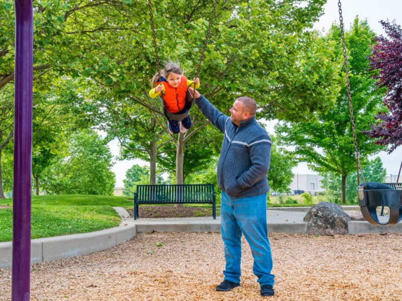 man pushing young boy on swings at Stone Creek Community Park playground